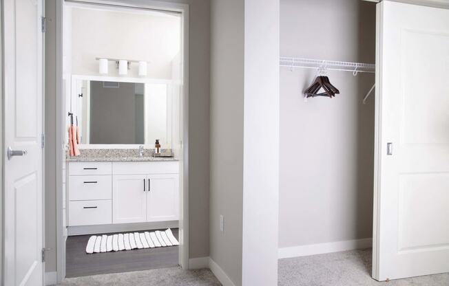 Modern apartment bathroom featuring stain-resistant floors and elegant granite countertops. The adjacent spare bedroom boasts plush carpeting and a spacious closet with sliding doors