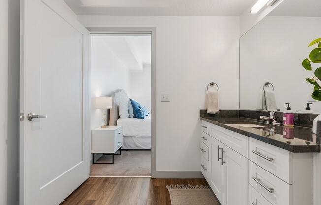 a bathroom with white cabinets and a mirror and a door to a bedroom