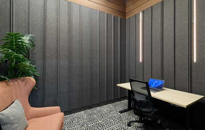 A modern office with a wooden desk, a black chair, and a pink armchair.