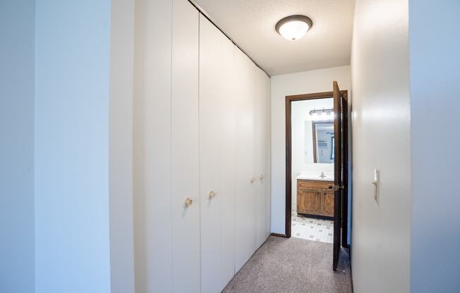 a hallway with white cabinets and a bathroom with a mirror.  Eagan, MN Glen Pond Apartments