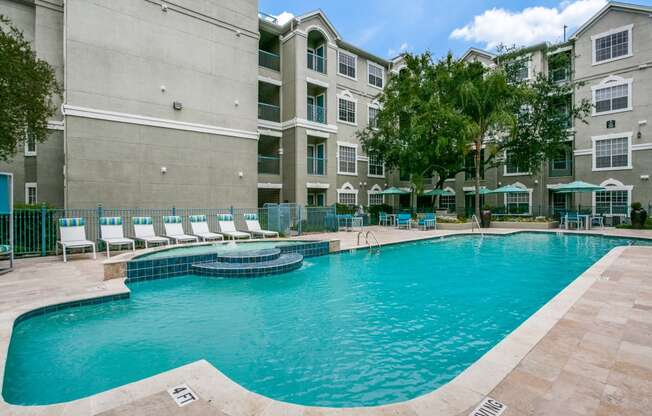 Houston Apartments for Rent - Large Enclosed Community Pool with Lounge Seating Surrounded by Greenery