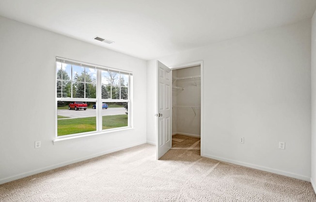A room with a carpeted floor, a window with a view of a street, and a door leading to another room.