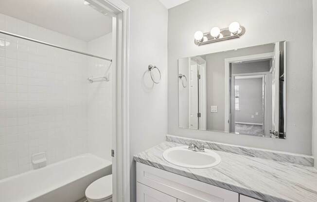 A white bathroom with a marble counter top and a white tub.
