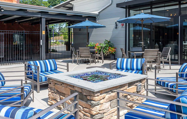 A patio with blue and white striped chairs and a stone fire pit.