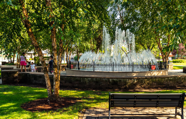 A fountain in a park with a bench in the foreground. at Vermella Lyndhurst apartments, New Jersey