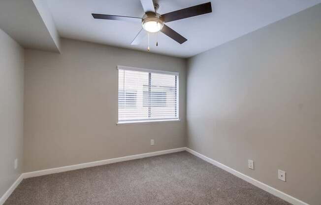 A room with a ceiling fan and a window with blinds.
