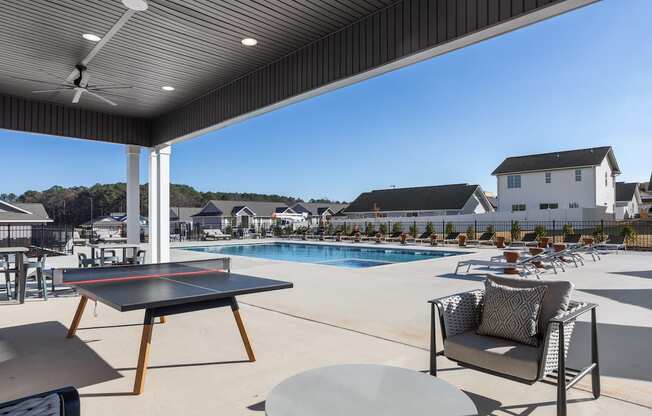 a large covered patio by the pool with ping pong and furniture at Sanctuary at Indian Creek rental homes in Madison, AL