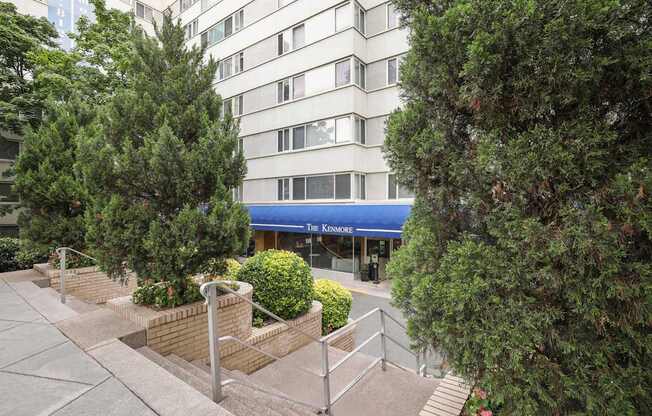 A view of a building with a blue awning and a tree in front of it.