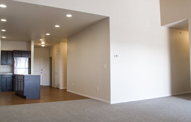 an empty living room with a kitchen in the background