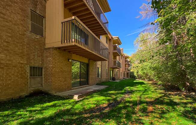 A sunny day at a brick apartment complex with green grass and trees.