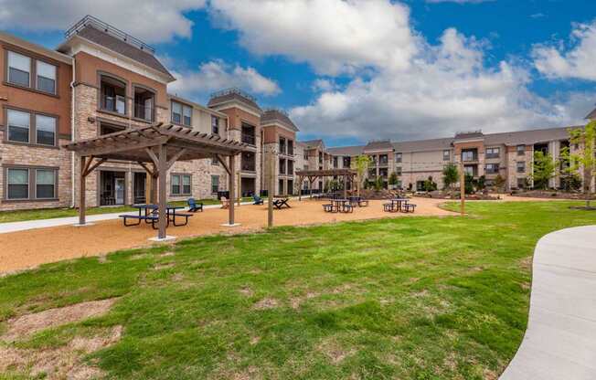 A large grassy area in front of apartment buildings with picnic tables.