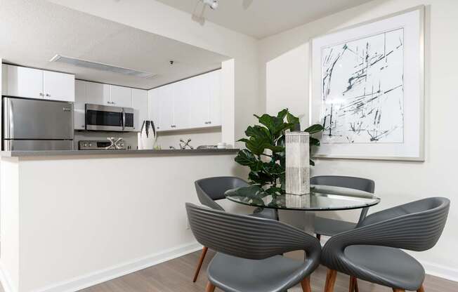 A modern kitchen with a glass dining table and grey chairs.