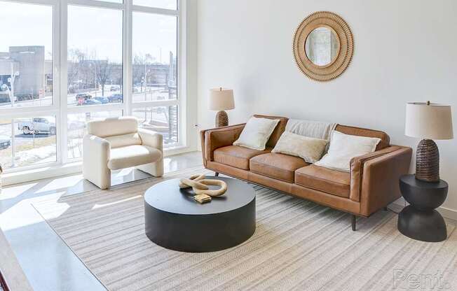 A living room with a brown couch, a white chair, and a round table with a yellow object on it.