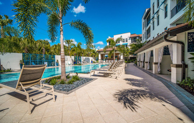 a pool with chairs and palm trees next to a building at Magnolia Square, Naples, FL