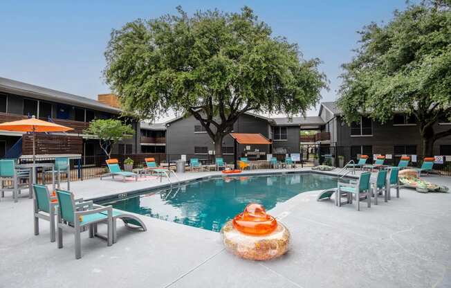 community swimming pool at Stadium 700 apartments in Arlington, TX with patio furniture and large trees.