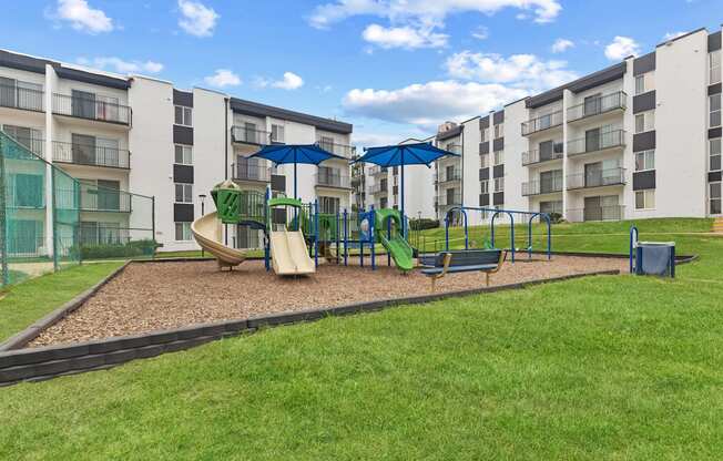 A playground with a green slide and a blue umbrella.