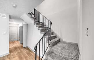 A staircase with a black railing and a grey carpeted stair runner.