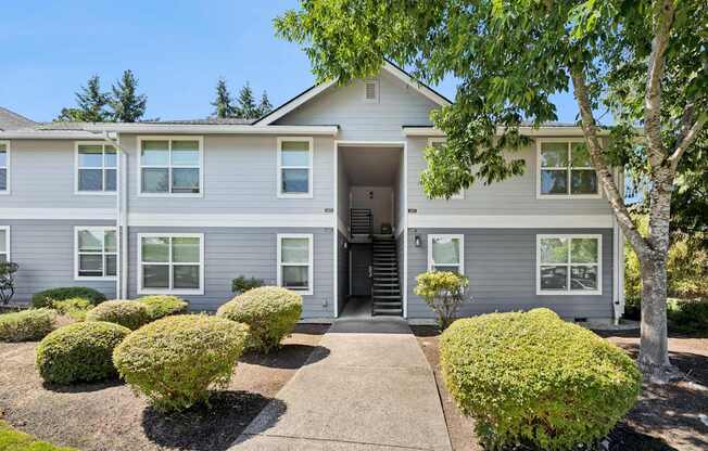 A grey house with a front yard and bushes.