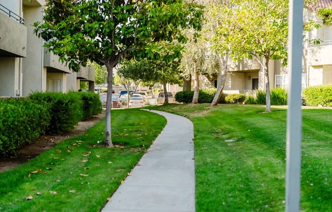 A concrete walkway leads through a grassy area between two apartment buildings.