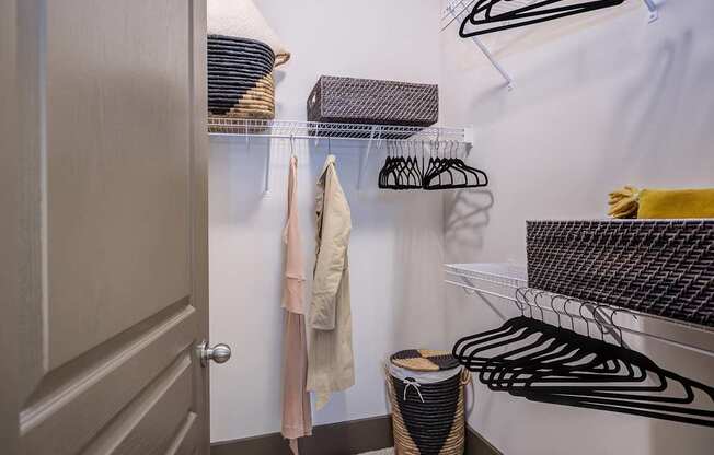 A closet with clothes hanging and a basket on the floor.