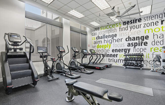 A gym with a variety of equipment and a motivational word cloud on the wall.