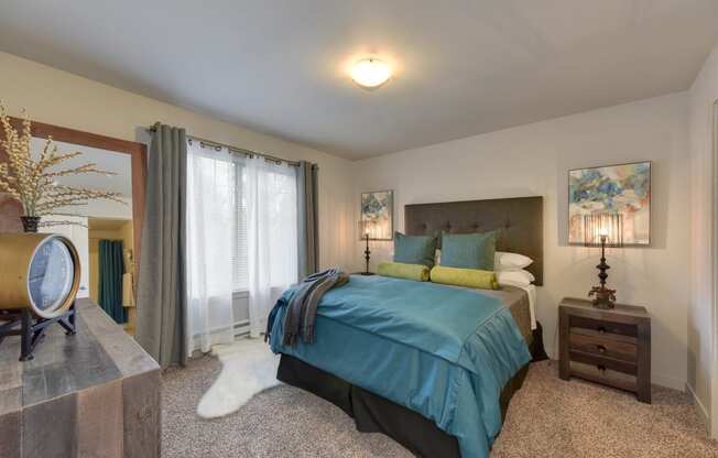 Master Bedroom with Kings Sized Mattress with Blue and Gray Comforter, Carpet, Wood Dressers with Lamp and Clock on top, and Open Window