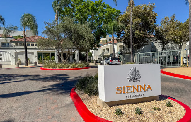 The image shows a sign for Sienna Residences in front of a gated community with palm trees and houses.
