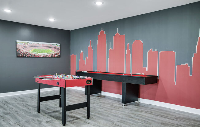a games room with two red tables and a skyline painted on the wall
