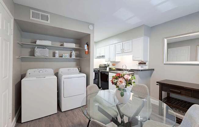 A laundry room with a washer and dryer, a dining table with chairs, and a kitchen area with cabinets and a countertop.