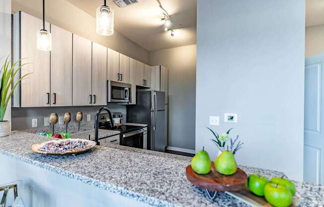 A kitchen with granite countertops and a tray of green apples.