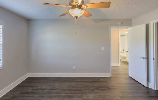 an empty living room with a ceiling fan and a door to a bathroom