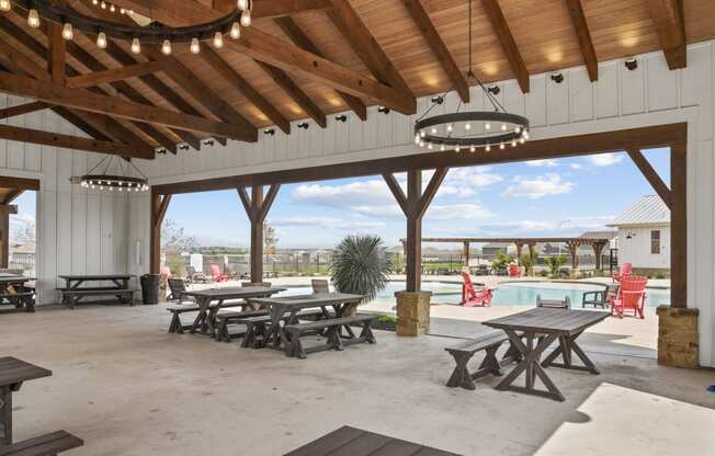 a covered patio with picnic tables and a pool in the background at Beacon at Presidential Heights, Texas, 78653
