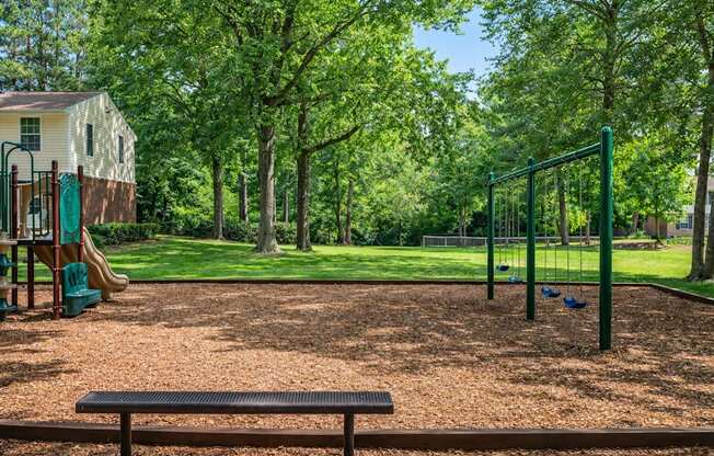 A playground with a green swing set and a brown bench.