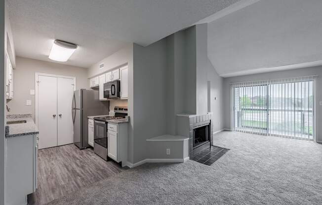 an empty living room and kitchen with a fireplace and a window