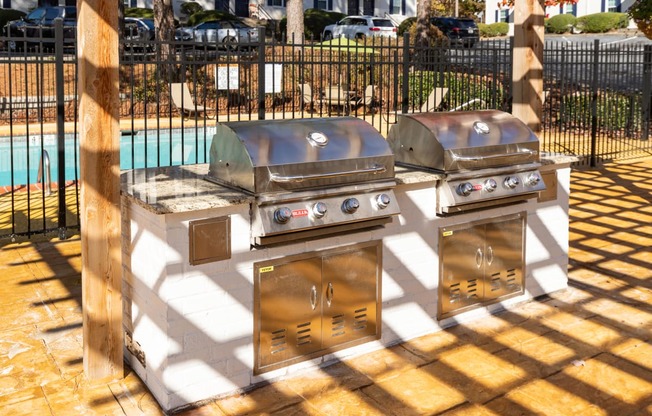 two bbq grills on a patio with a pool in the background