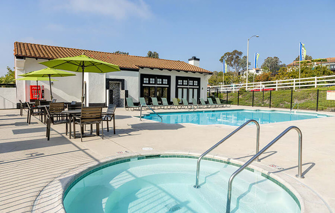 A pool with a ladder and a table with chairs and an umbrella outside a building.
