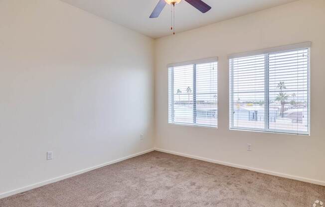A room with a ceiling fan and two windows.