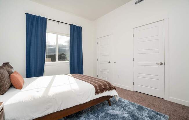 A bedroom with a large bed and a window with blue curtains.