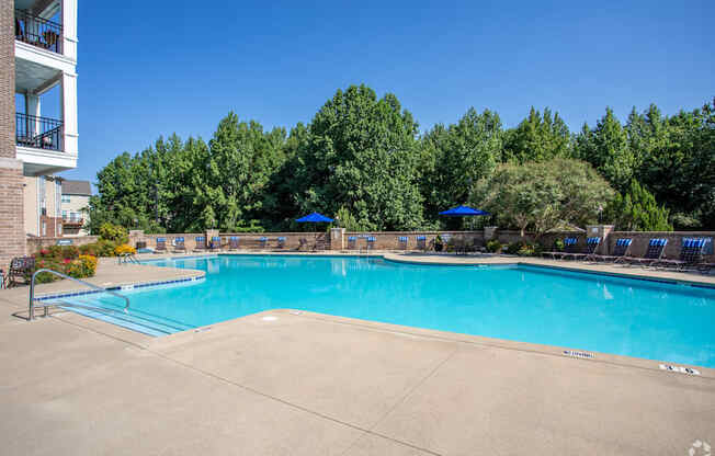 A large swimming pool surrounded by trees and chairs.