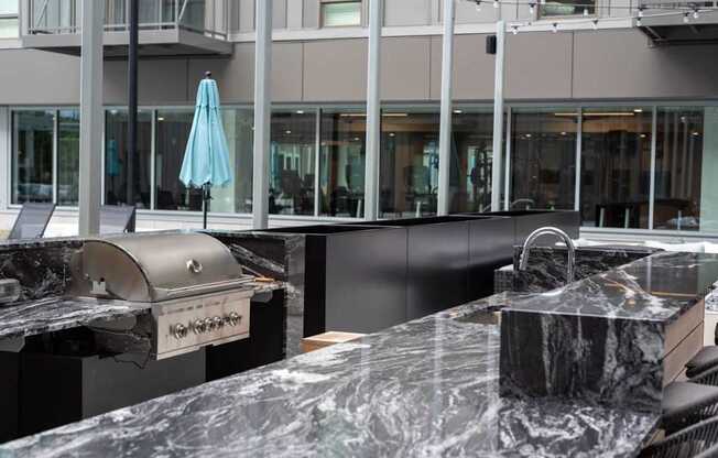 A marble countertop with a grill and umbrella in the background.