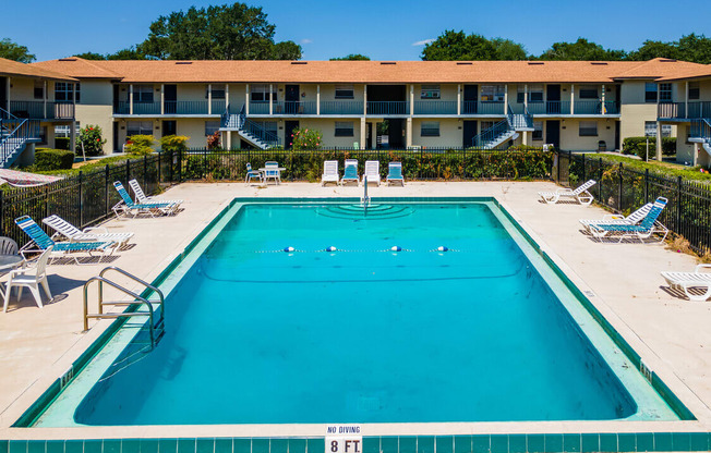 A swimming pool in front of a building with lounge chairs around it.