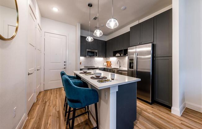 A kitchen with an island, stainless steel appliances, hardwood-style flooring and pendant lights.