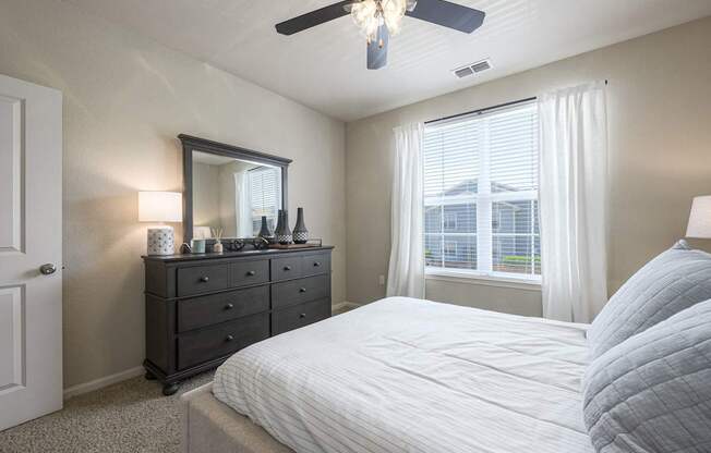 A bedroom with a large bed, a dresser with a mirror, and a ceiling fan.