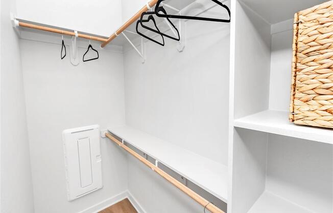 Walk-in closet with built-in shelving, three clothes rods, a fuse box, hangers, and a basket