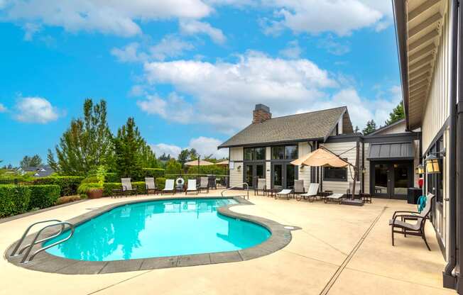 a swimming pool with lounge chairs and umbrellas in front of a house