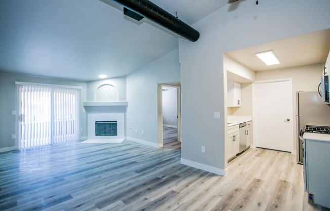 an empty living room with a fireplace and kitchen in the background