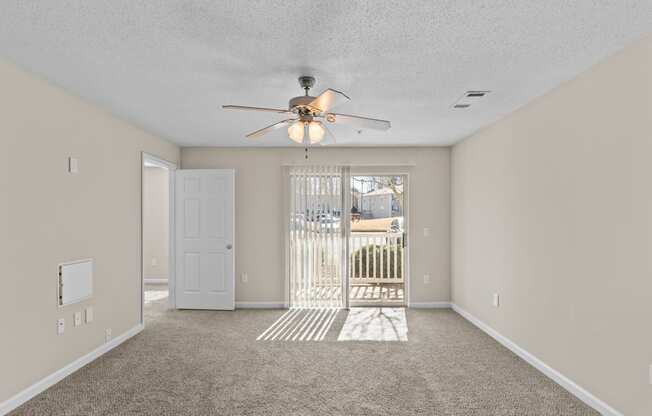 an empty living room with a ceiling fan and a door to a balcony
