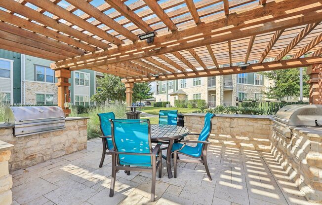 A wooden pergola with a table and chairs is set up on a patio.