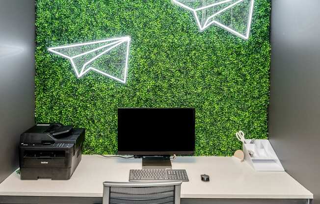 a desk with a computer and a chair in front of a wall covered in green plants