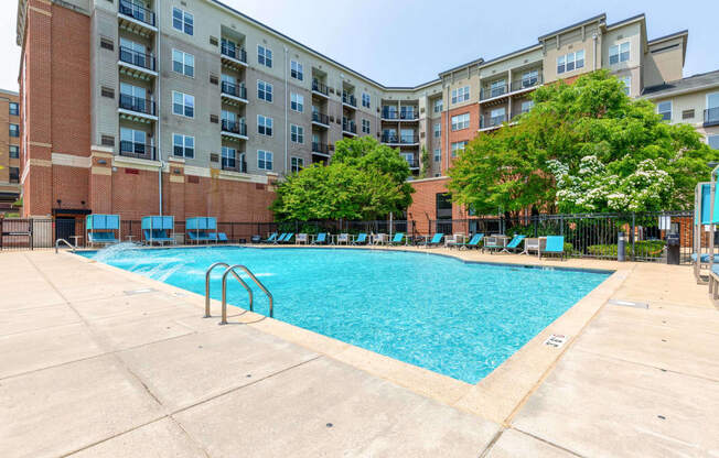 an outdoor swimming pool with chaise lounge chairs and an apartment building in the background